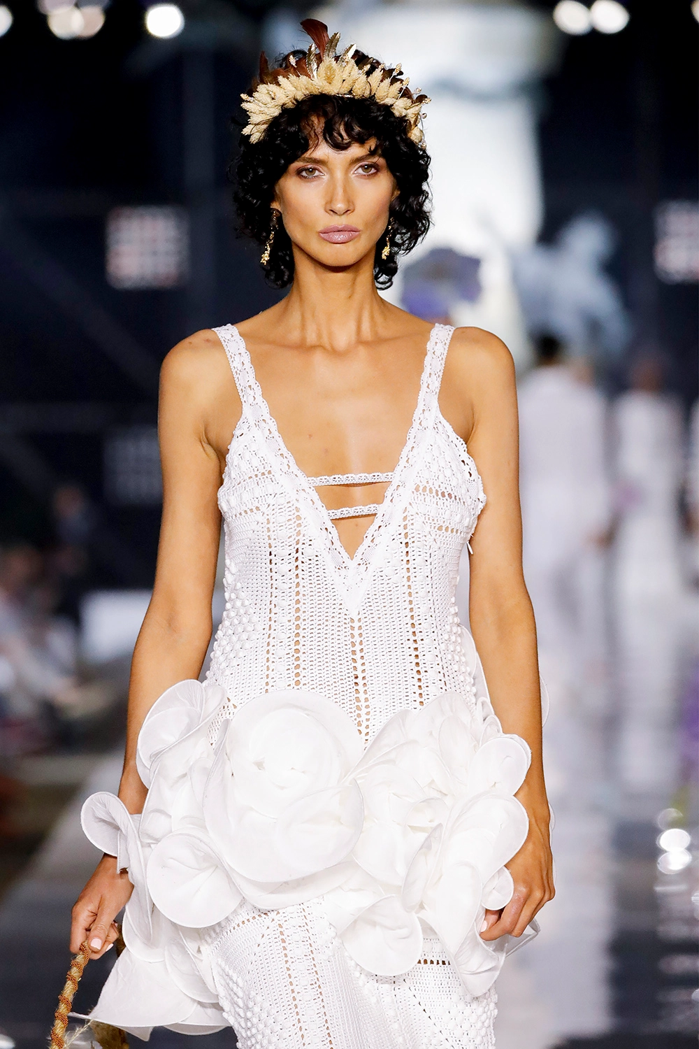 Modelo con vestido blanco de ganchillo y flores de tela en la pasarela